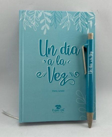 ** Imagen de una libreta turquesa titulada "Un Día a la Vez" acompañada de un bolígrafo del mismo color.