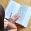 Niña concentrada leyendo un libro en un piso de madera