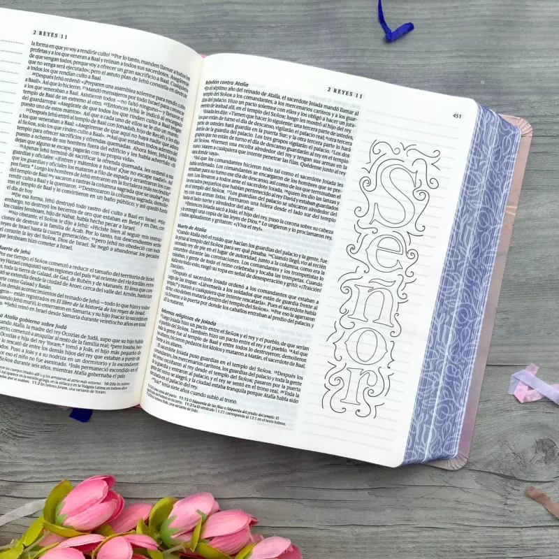 ** Biblia abierta sobre una mesa de madera con la palabra "Señor" decorada en la página. Al lado, flores rosadas.