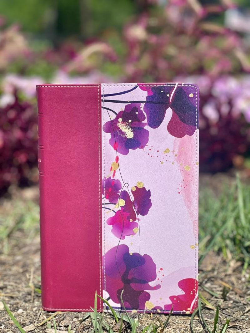 ** Funda de tono rosa con diseño floral morado y rosa sobre un fondo natural.