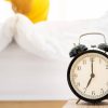 Reloj despertador clásico junto a una cama con persona despertando.