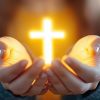 Manos sosteniendo una cruz iluminada, simbolizando la fe y la esperanza.