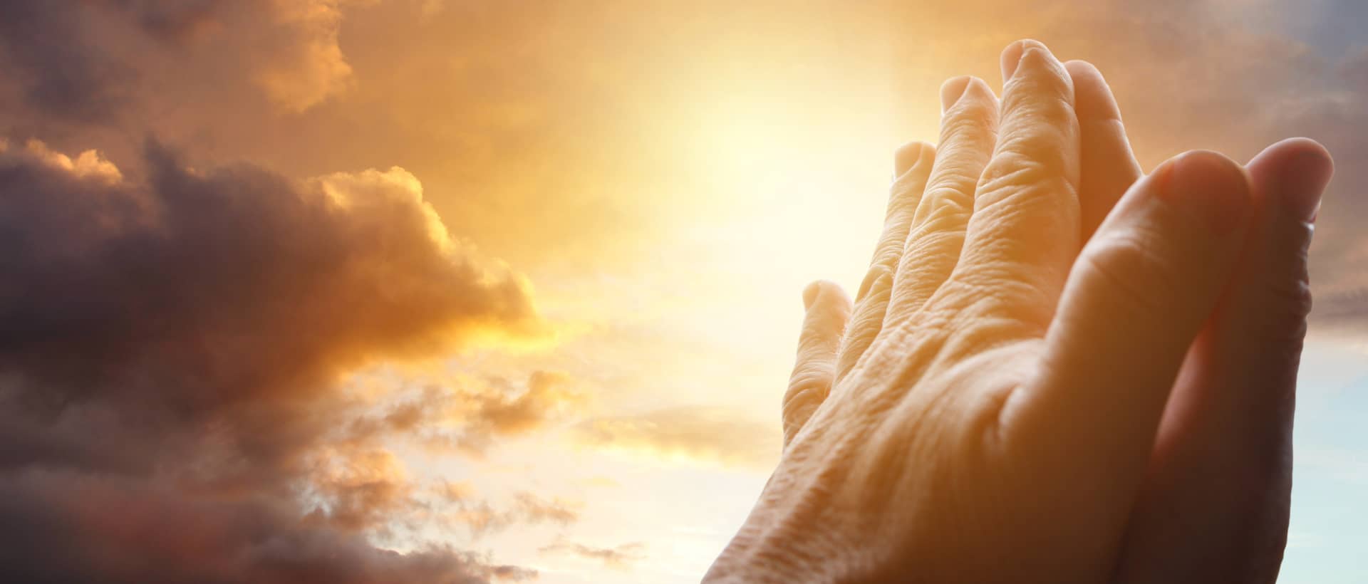 Manos unidas en oración bajo un cielo iluminado por el amanecer.