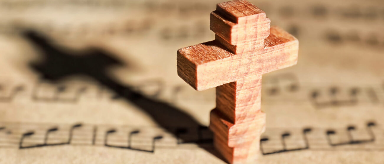 El perdón sin límites: ¿Qué significa “70 veces 7” en la Biblia? 5 Cruz de madera sobre partituras musicales, con sombra de la forma de una cruz” Título: “El perdón de la cruz