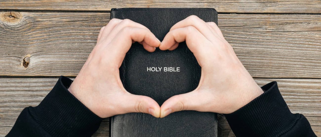 Manos en forma de corazón sobre la Santa Biblia