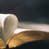 Persona sosteniendo una cruz frente al sol con una Biblia abierta