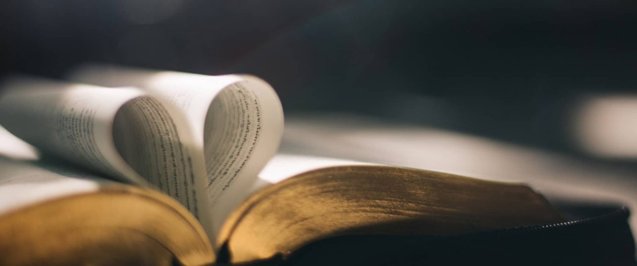 Persona sosteniendo una cruz frente al sol con una Biblia abierta