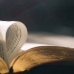 Persona sosteniendo una cruz frente al sol con una Biblia abierta