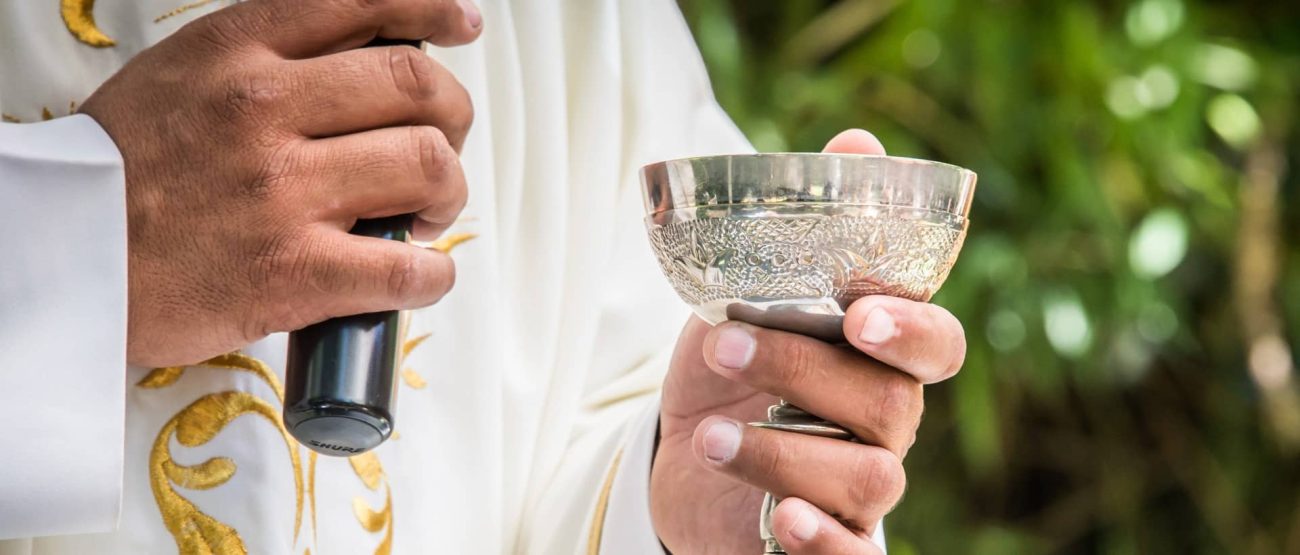 Sacerdote sosteniendo el cáliz y el micrófono durante una celebración eucarística al aire libre.